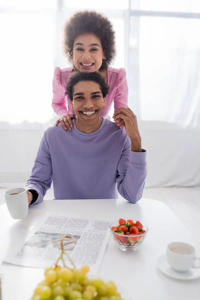 Young african american couple smiling at camera near drinks, fruits and newspaper at home — Stock Photo