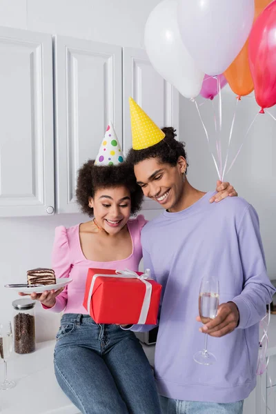Felice coppia afroamericana con torta, champagne e regalo in cucina — Foto stock