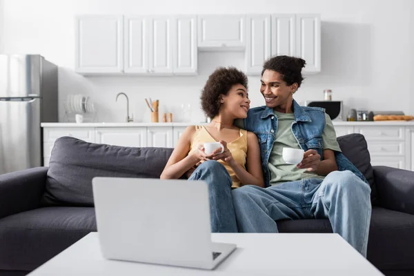 Young african american couple holding cups near laptop at home — Stock Photo