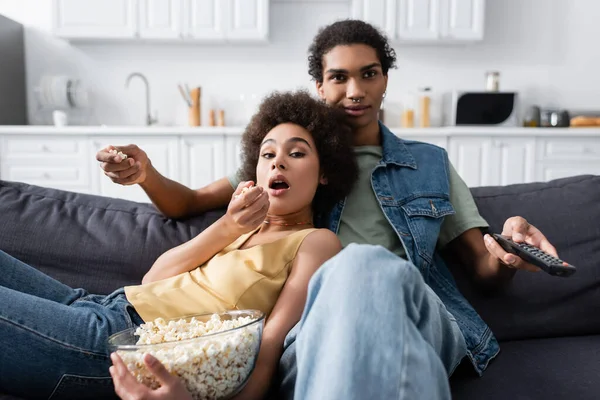 Young african american couple holding popcorn while watching film on couch at home — Foto stock