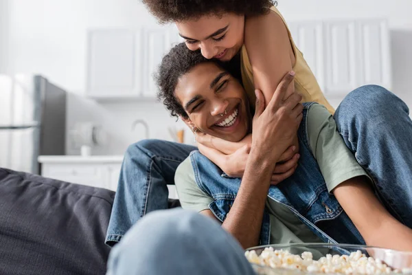 Jovem mulher afro-americana abraçando namorado perto de pipocas borradas no sofá — Fotografia de Stock