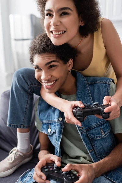 KYIV, UCRANIA - 9 de noviembre de 2021: Pareja afroamericana alegre jugando videojuegos en casa - foto de stock