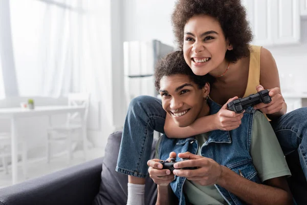 KYIV, UCRANIA - 9 de noviembre de 2021: Mujer afroamericana enfocada jugando videojuegos con su novio en casa - foto de stock