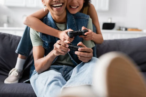 KYIV, UCRANIA - 9 de noviembre de 2021: Vista recortada de una pareja afroamericana sonriente jugando videojuegos en casa - foto de stock