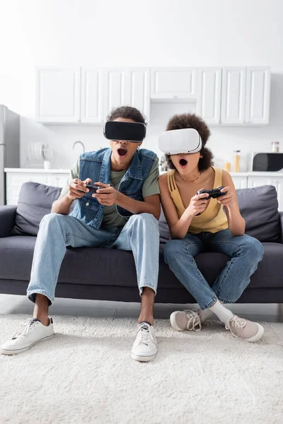 KYIV, UKRAINE - 9 NOVEMBRE 2021 : Couple afro-américain choqué dans un casque vr jouant à un jeu vidéo à la maison — Photo de stock