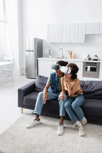 Couple afro-américain excité dans des casques vr assis sur le canapé à la maison — Photo de stock