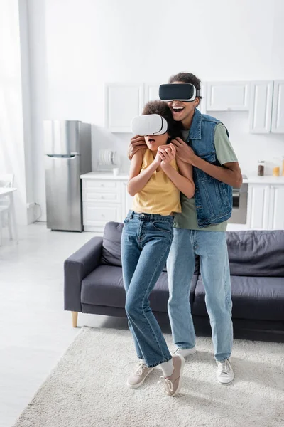 Smiling african american man hugging scared girlfriend in vr headset at home — Fotografia de Stock