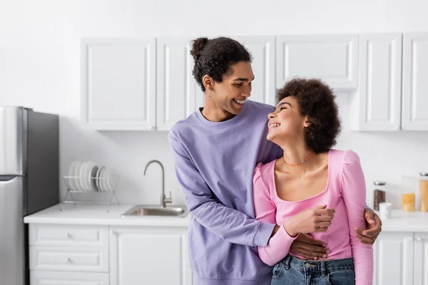 Молода афроамериканська пара дивиться один на одного, обіймаючись у кухні. — стокове фото