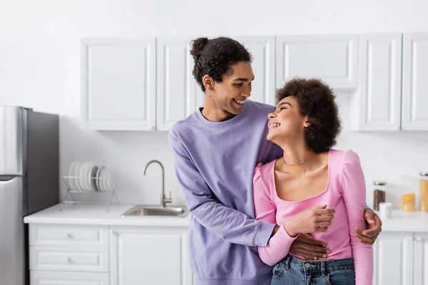 Jovem casal afro-americano olhando um para o outro enquanto abraça na cozinha — Fotografia de Stock