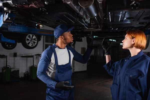 Vue latérale de la mécanique interracial pointant vers l'automobile dans le service de voiture — Photo de stock