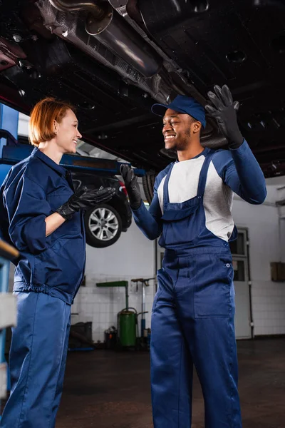 Positive interracial mechanics talking under car in service — Stockfoto