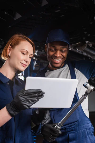 Multiethnic mechanics with digital tablet and wrench standing near car in garage — Stock Photo