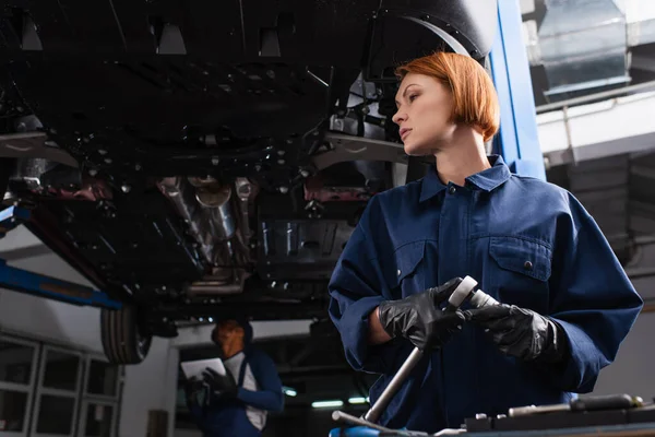 Niedrigwinkel-Ansicht der Arbeiterin mit Schraubenschlüssel in der Nähe von Auto in der Garage — Stockfoto