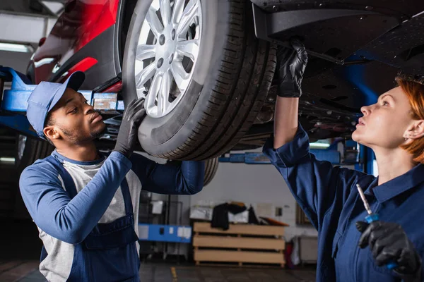 Interracial mechanics in uniform working with car wheel in garage — Foto stock