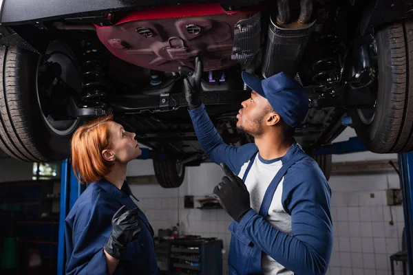 Vue latérale de la mécanique interracial regardant le fond de la voiture en service — Photo de stock