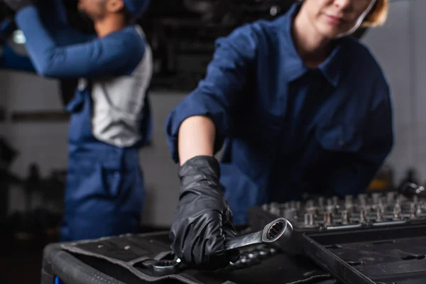 Ausgeschnittene Ansicht eines Mechanikers, der Schraubenschlüssel in der Nähe verschwommener afrikanisch-amerikanischer Kollege im Autoservice nimmt — Stockfoto