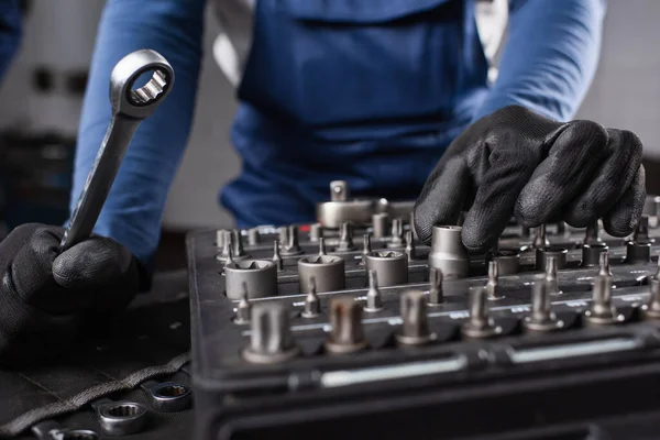 Обрізаний вид механіка в рукавичках, що тримає ключ біля інструментів в гаражі — стокове фото