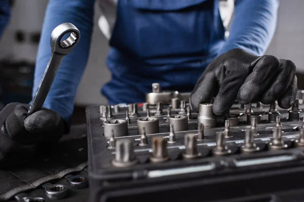 Cropped view of mechanic in gloves holding wrench near tools in garage — стоковое фото