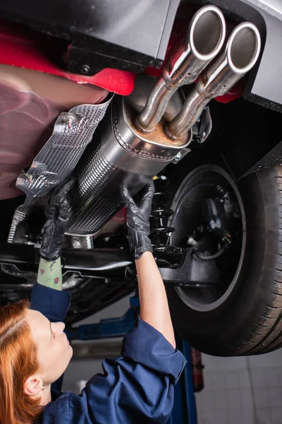 Pelirroja trabajadora en uniforme trabajando con coche en garaje - foto de stock