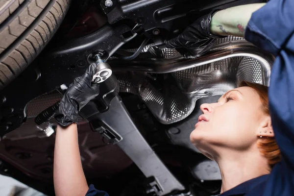 Vista de ángulo bajo del mecánico trabajando con llave inglesa y coche en el garaje - foto de stock