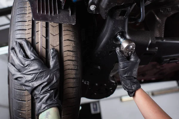 Vista recortada de mecánico en guantes trabajando con llave inglesa cerca de rueda de coche en garaje - foto de stock