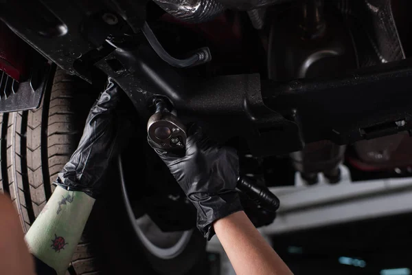 Vista recortada de la trabajadora en guantes trabajando con llave inglesa y auto en garaje - foto de stock