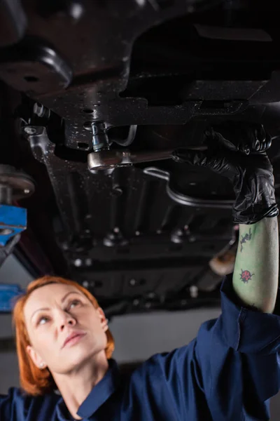 Verschwommene Arbeiterin arbeitet mit Schraubenschlüssel unter Auto in Garage — Stockfoto