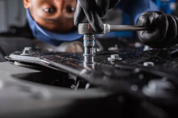 Vista recortada de trabajador afroamericano usando llave inglesa en coche en garaje - foto de stock