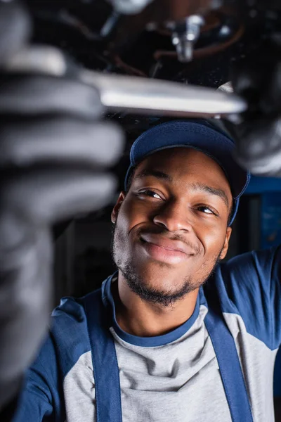 Contremaître afro-américain souriant travaillant sous voiture en service — Photo de stock