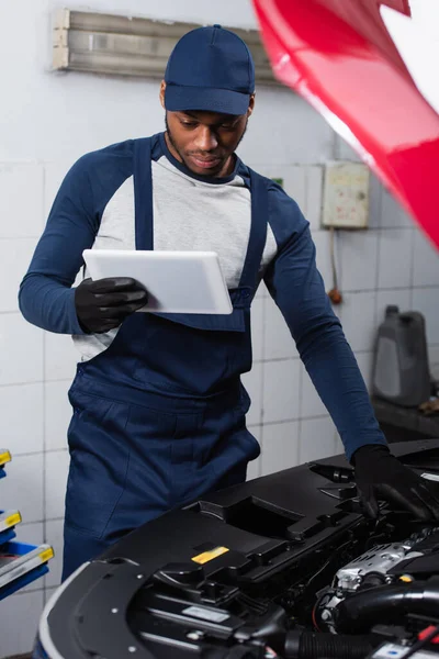 African american technician with digital tablet making diagnostics of car in workshop — Foto stock