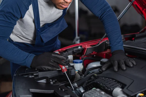 Partial view of african american technician in work gloves inspecting car engine compartment with screwdriver — Foto stock