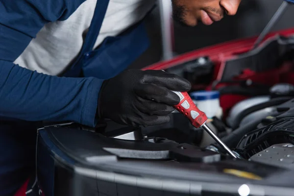 Partial view of african american mechanic with screwdriver fixing car engine in workshop — Fotografia de Stock