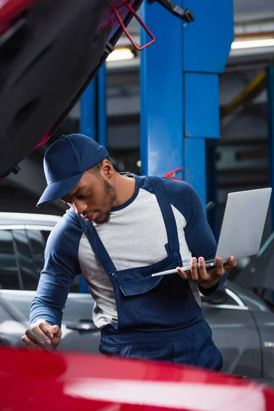 Capataz americano africano fazendo diagnósticos de carro embaçado enquanto segurando laptop — Fotografia de Stock