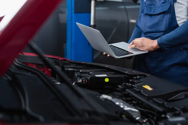 Vue partielle du contremaître afro-américain avec ordinateur portable faisant des diagnostics de voiture floue — Photo de stock