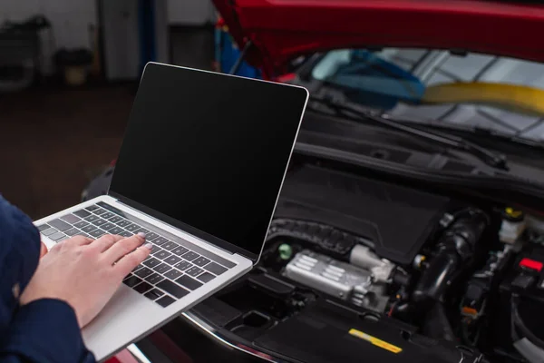 Ausgeschnittene Ansicht eines Mechanikers mit Laptop mit leerem Bildschirm in der Nähe eines verschwommenen Autos in der Werkstatt — Stockfoto