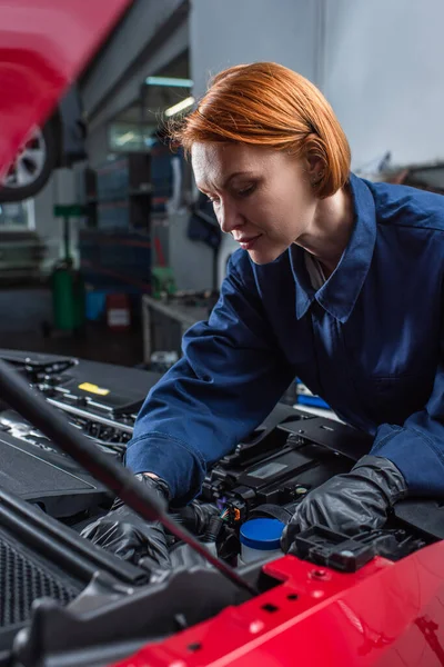 Technician in uniform checking car engine compartment in service station — Foto stock