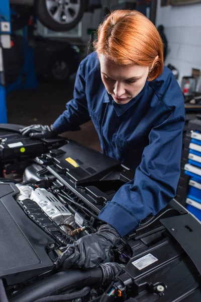 Mechanic in uniform and work gloves inspecting motor of car in service station — Foto stock