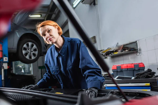 Frau in Uniform blickt in Werkstatt in Kamera neben verschwommenem Auto — Stockfoto