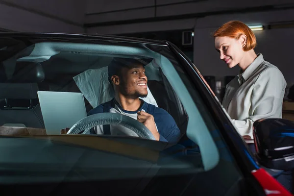 Smiling african american foreman with laptop making diagnostics of car near pleased client — Stock Photo