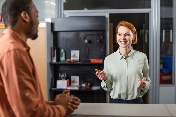 Positiver Autohändler gestikuliert, während er mit verschwommenem afrikanisch-amerikanischen Mann spricht — Stockfoto