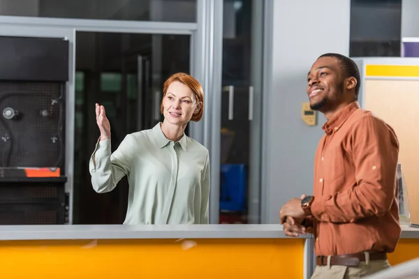 Car dealer pointing with hand near pleased african american man — стоковое фото