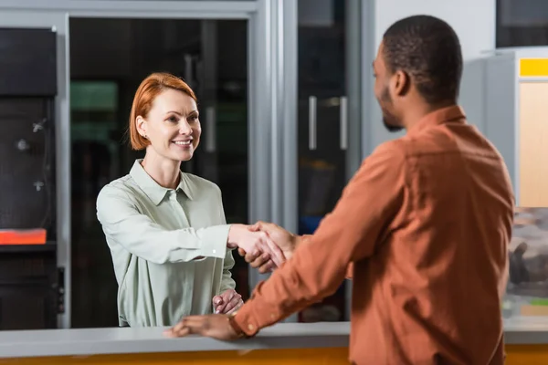 Smiling car dealer shaking hands with blurred african american customer — Stock Photo