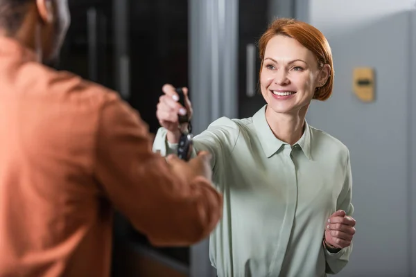 Pleased car dealer giving key to blurred african american client — Stock Photo
