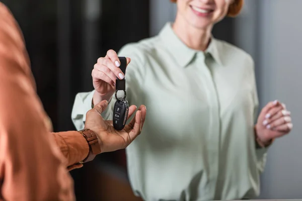 Cropped view of smiling car dealer giving key to blurred african american man — Foto stock