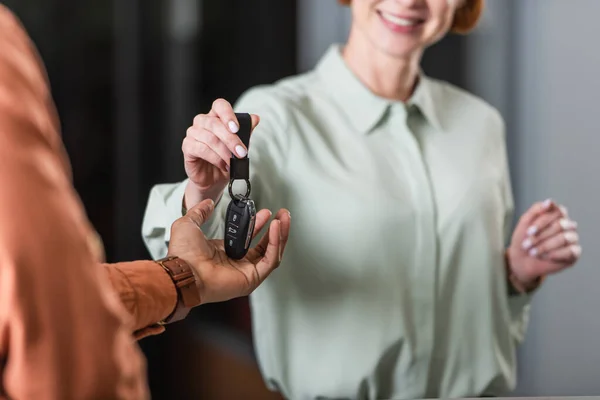 Cropped view of smiling car dealer giving key to blurred african american man — Stock Photo