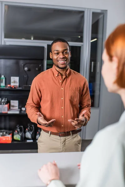 Souriant afro-américain concessionnaire de voitures parler à son client sur le premier plan flou — Photo de stock