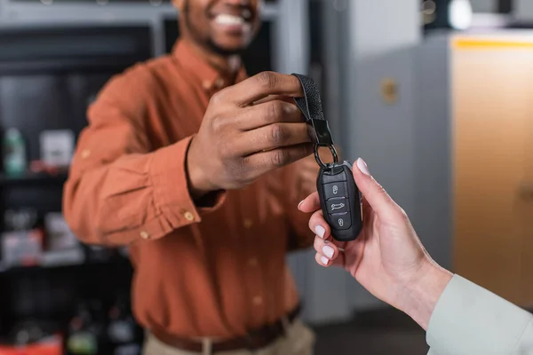 Partial view of woman taking key from african american car dealer smiling on blurred background — Stock Photo