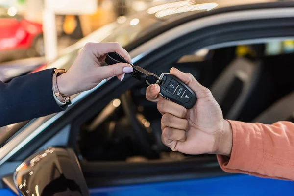 Partial view of car dealer giving key to african american client near blurred car — Fotografia de Stock