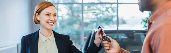 Happy car dealer giving key to african american client of car service, banner — Stock Photo