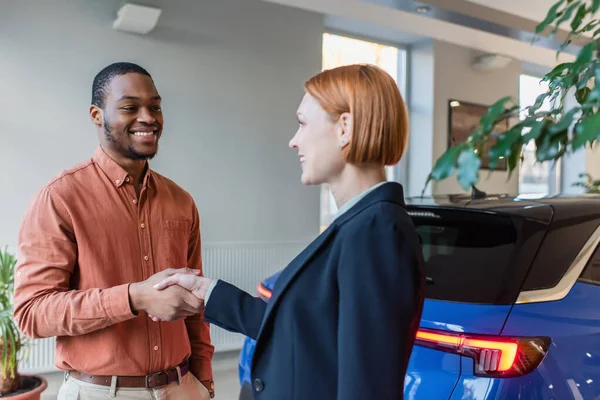 Happy african american man and car dealer shaking hands near car — Foto stock